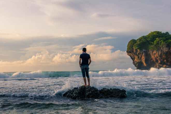 man standing on stone near seashore during sunrise photography